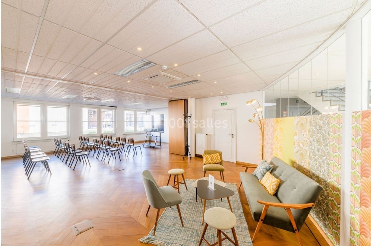 Salle lumineuse avec parquet, chaises alignées pour une réunion et coin salon avec canapé, fauteuils et tables basses.