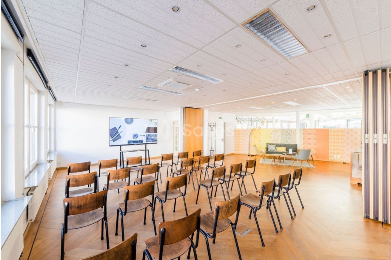 Salle lumineuse avec chaises en bois disposées face à un écran, parquet au sol et cloisons décoratives en arrière-plan.