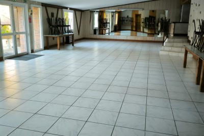 Salle vide avec sol carrelé blanc, murs décorés de bois, miroirs et portes vitrées donnant sur l'extérieur.