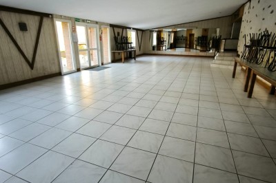 Salle vide avec sol carrelé blanc, murs décorés de bois, miroirs et portes vitrées donnant sur l'extérieur.