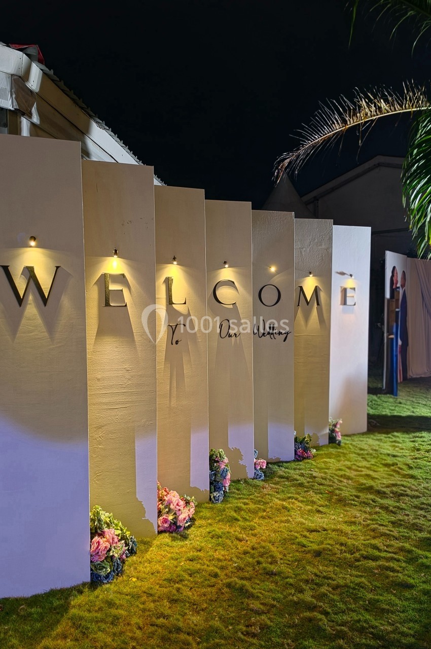 Panneaux lumineux alignés avec le mot ’WELCOME’, décorés de fleurs, sur une pelouse éclairée de nuit.