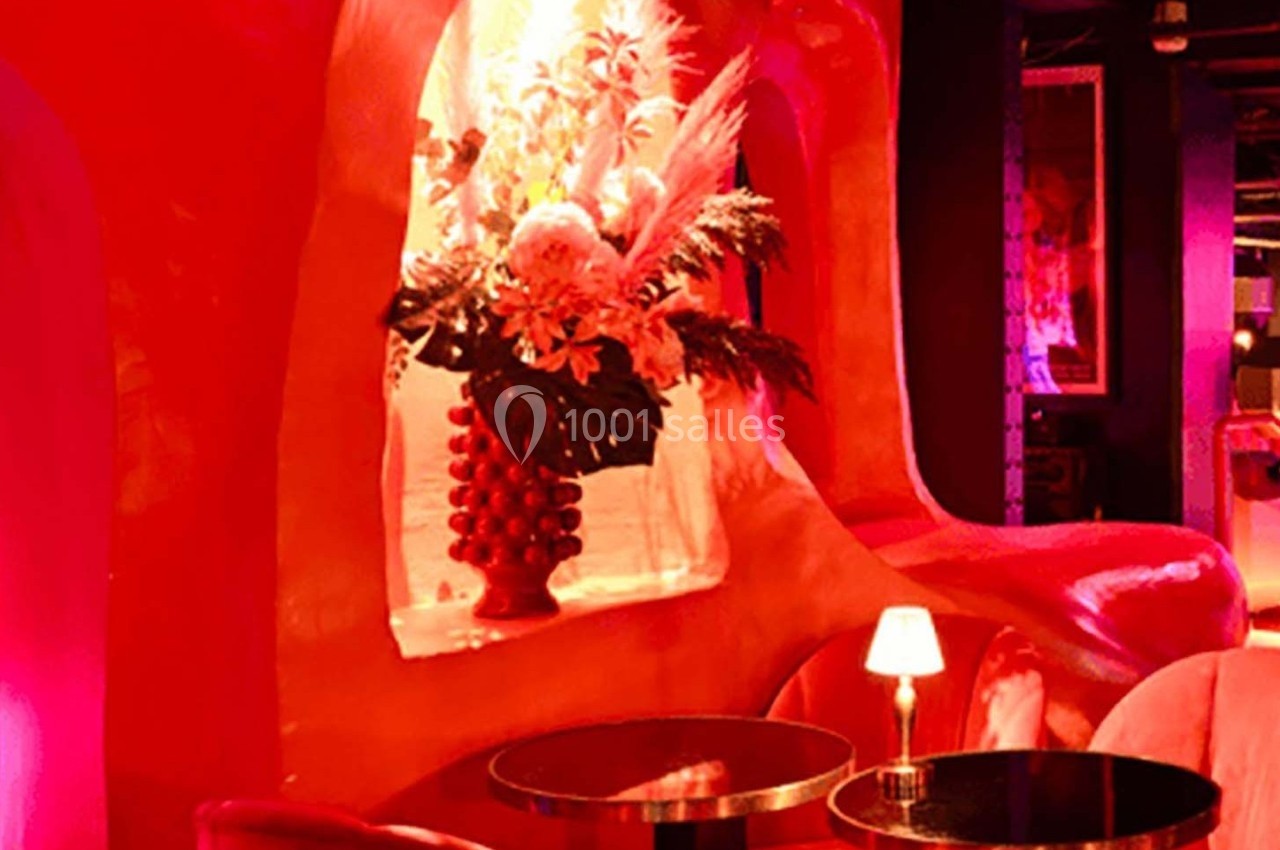 Décor intérieur avec fauteuils rouges, table basse, lampe allumée et composition florale dans une niche éclairée.