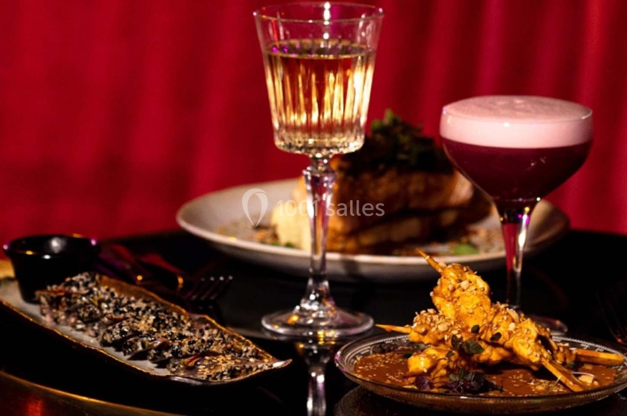 Assortiment de plats gastronomiques avec deux cocktails sur une table, devant un fond rouge.