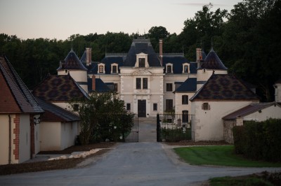 Chambre avec lit double, poutres apparentes, linge de lit blanc, et salle de bain attenante visible par une porte ouverte.