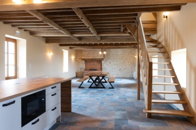 Chambre avec lit double, poutres apparentes, linge de lit blanc, et salle de bain attenante visible par une porte ouverte.