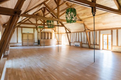 Chambre avec lit double, poutres apparentes, linge de lit blanc, et salle de bain attenante visible par une porte ouverte.