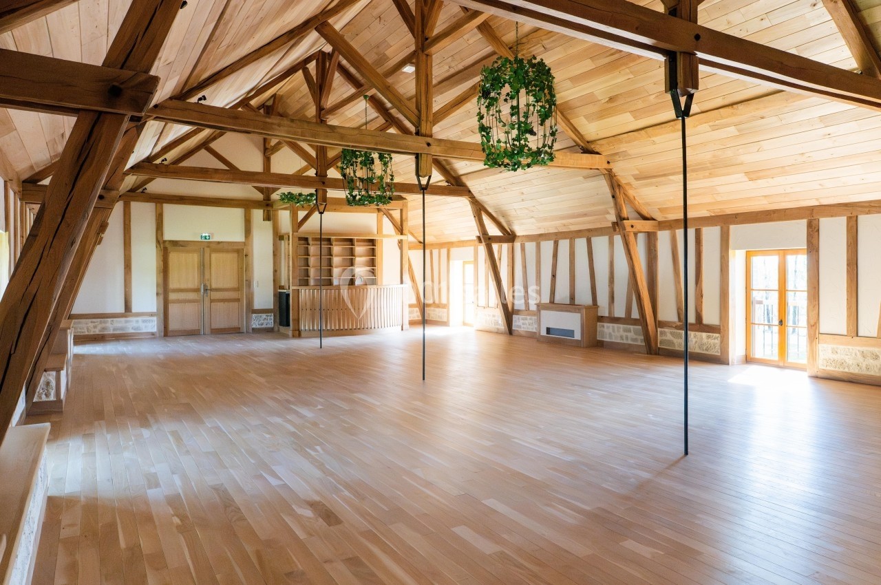 Grande salle lumineuse avec parquet en bois clair, charpente apparente et murs en bois et pierre.