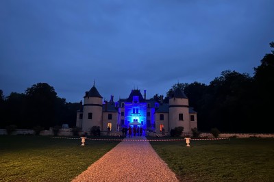 Chambre avec lit double, poutres apparentes, linge de lit blanc, et salle de bain attenante visible par une porte ouverte.