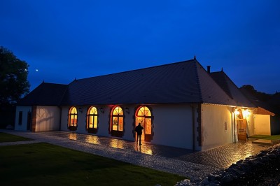 Chambre avec lit double, poutres apparentes, linge de lit blanc, et salle de bain attenante visible par une porte ouverte.