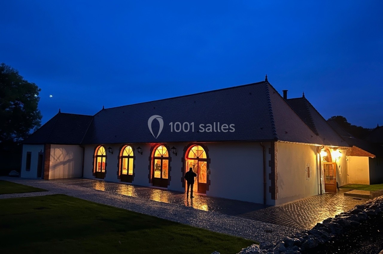 Bâtiment éclairé de nuit avec des fenêtres en arche, entouré d'une allée pavée et d'espaces verts.