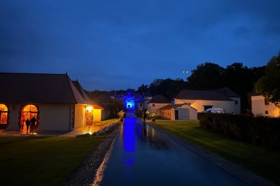 Chambre avec lit double, poutres apparentes, linge de lit blanc, et salle de bain attenante visible par une porte ouverte.