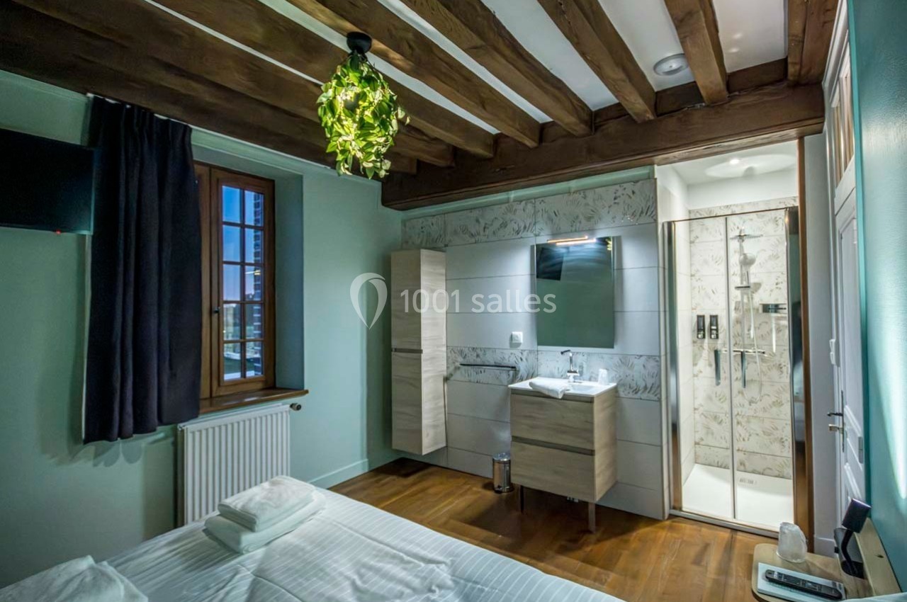 Chambre avec lit double, salle de bain attenante, poutres apparentes, parquet et décoration moderne.