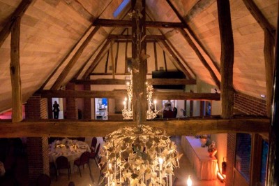 Chambre avec lit double, poutres apparentes, linge de lit blanc, et salle de bain attenante visible par une porte ouverte.