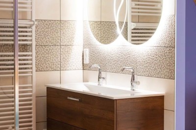 Chambre avec lit double, poutres apparentes, linge de lit blanc, et salle de bain attenante visible par une porte ouverte.