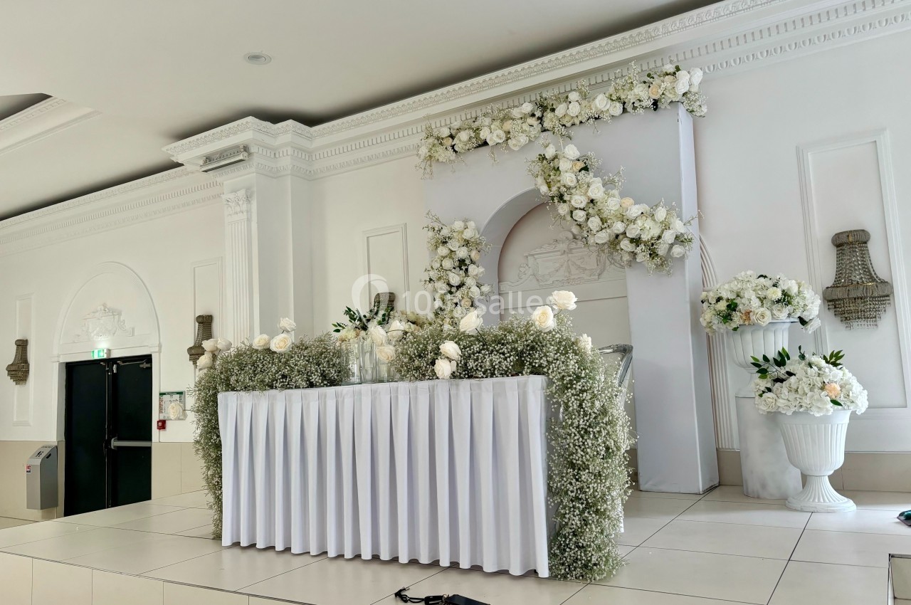 Table décorée de fleurs blanches et de gypsophiles sur une estrade dans une salle de réception élégante.