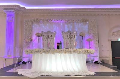 Salle de réception élégante avec tables dressées, lustres scintillants et éclairage coloré sur une scène.