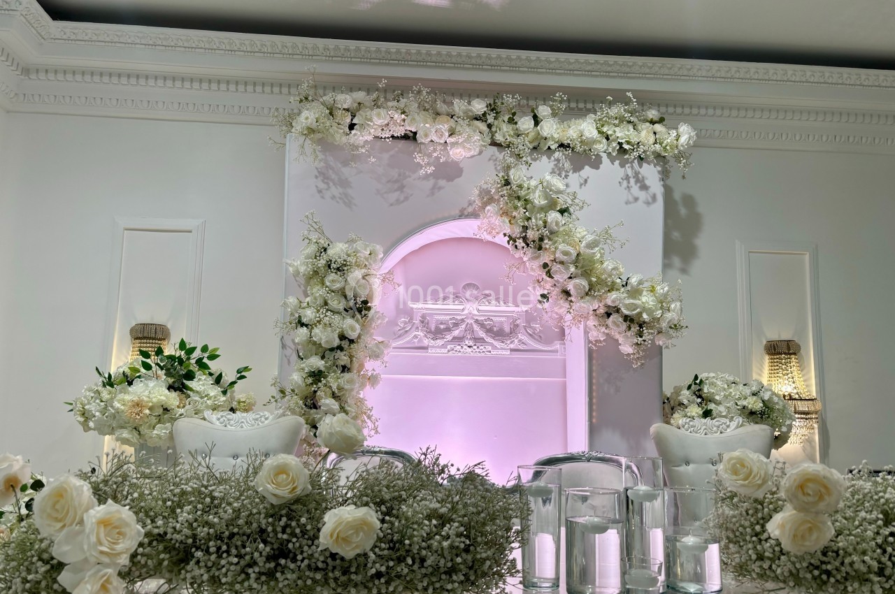 Décoration florale blanche élégante avec des roses et du gypsophile, encadrant une arche lumineuse dans une salle raffinée.