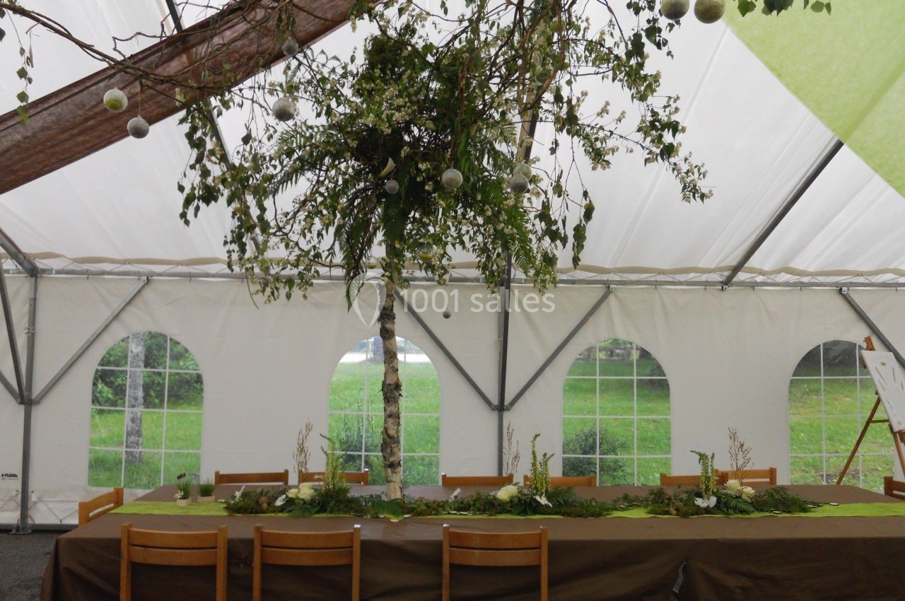 Décoration de table sous une tente, avec un arbre central orné de feuillages et de boules suspendues.