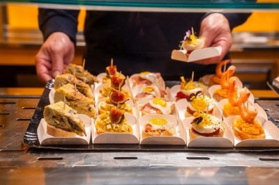 Assortiment de tapas variés présentés sur un comptoir, avec une personne servant en arrière-plan.