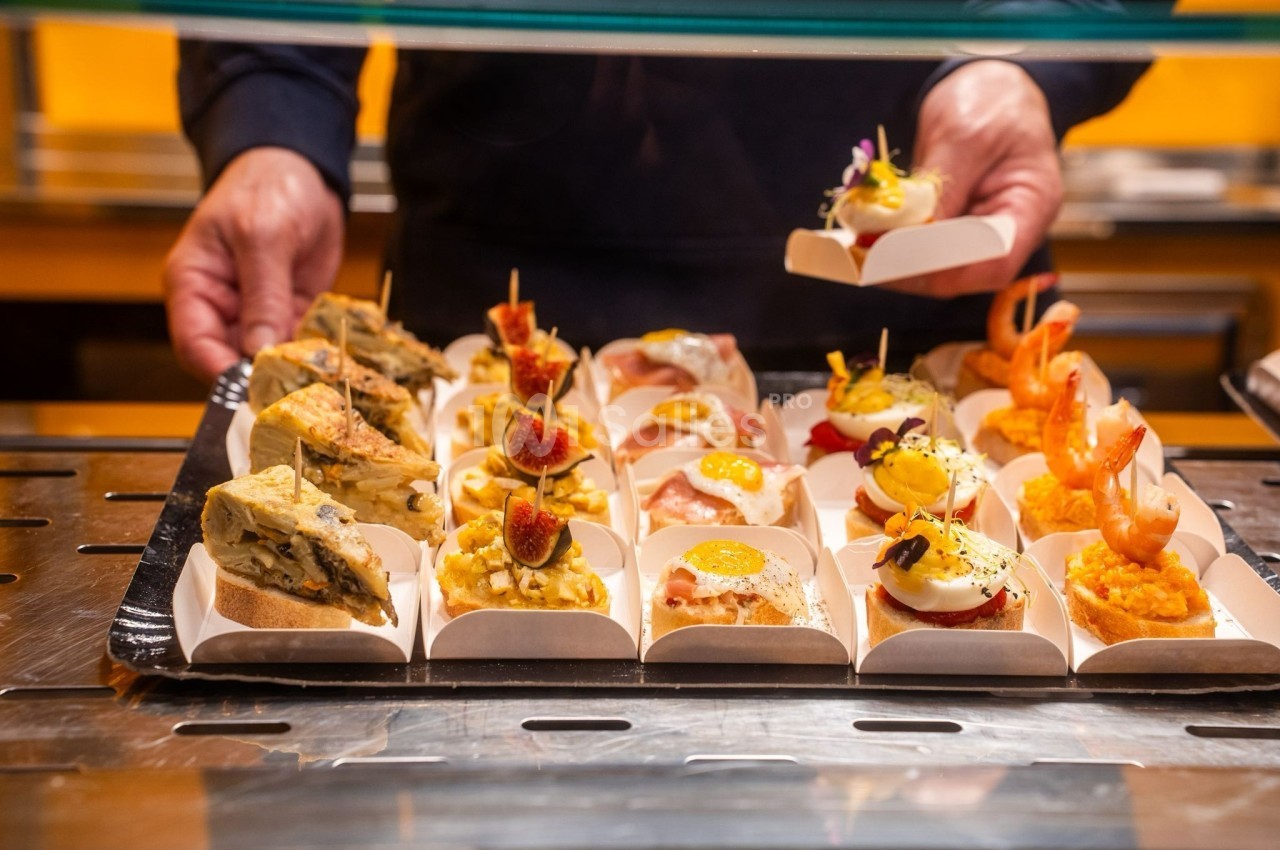 Assortiment de tapas variés présentés sur un comptoir, avec des mains ajustant les plats.