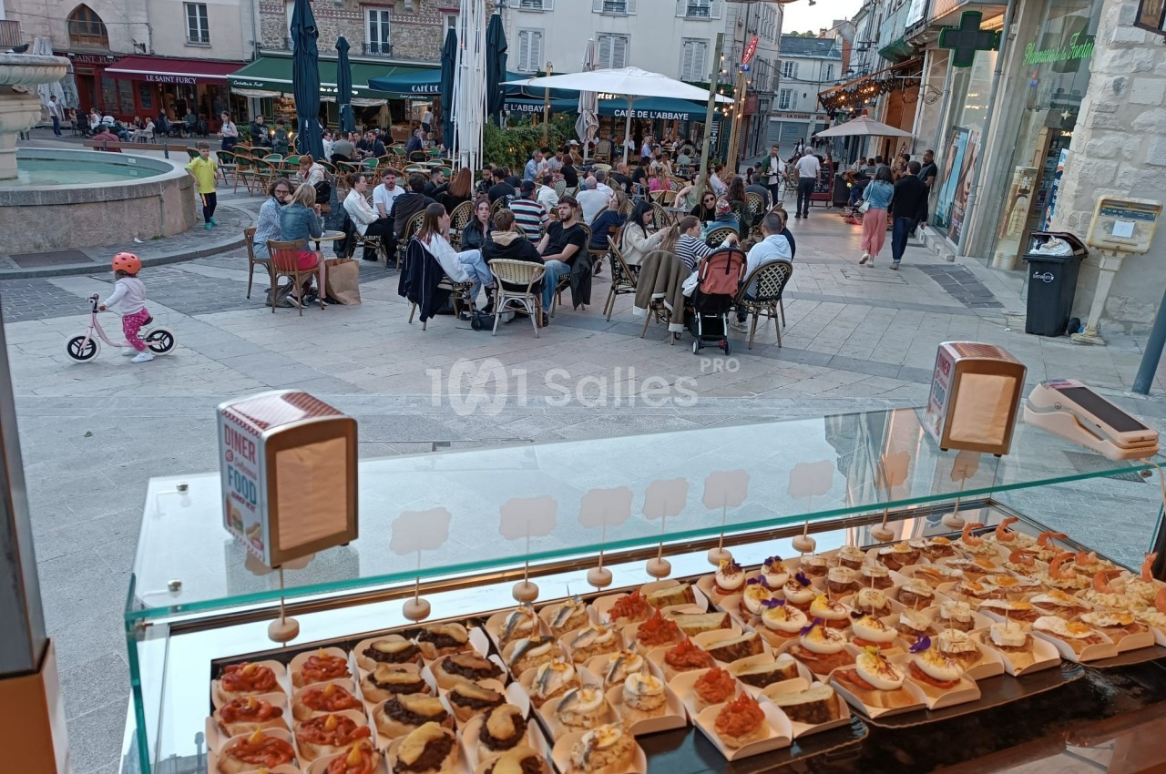 Vue d'un étal de tapas en vitrine avec une terrasse animée et une place publique en arrière-plan.