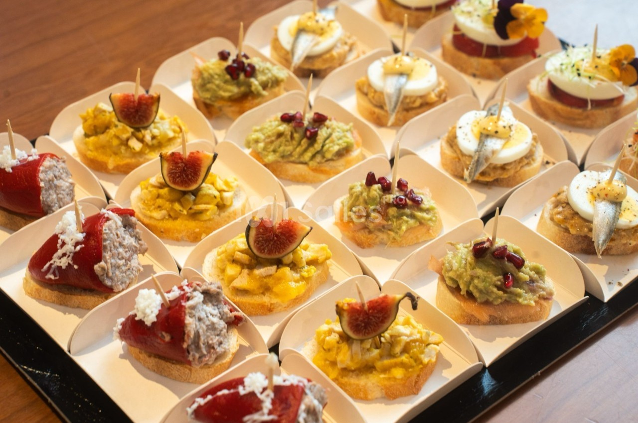 Plateau de tapas variées comprenant des toasts garnis d'avocat, figues, anchois, œufs et poivrons farcis.