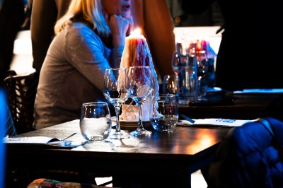 Table de restaurant avec bougie fondue allumée, verres à vin et serviette pliée, ambiance chaleureuse et tamisée.
