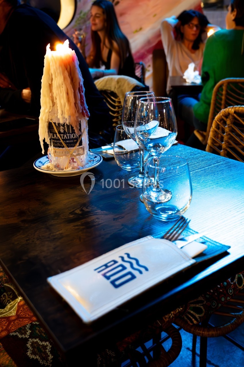 Table de restaurant avec bougie fondue allumée, verres à vin et serviette pliée, ambiance chaleureuse et tamisée.