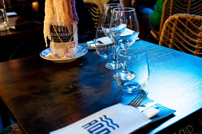 Vue d'un littoral avec une mer calme, un quai, des drapeaux et des collines à l'horizon sous un ciel dégagé.