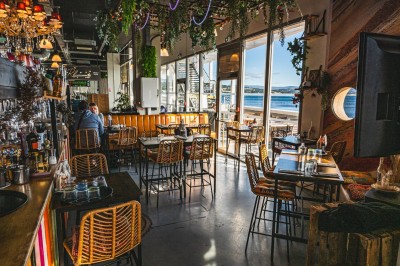 Vue d'un littoral avec une mer calme, un quai, des drapeaux et des collines à l'horizon sous un ciel dégagé.