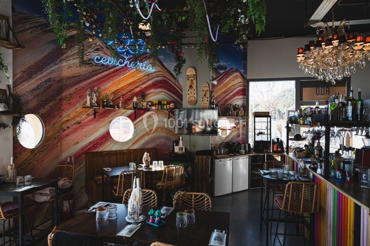 Intérieur d'un restaurant coloré avec décoration murale artistique, plantes suspendues et mobilier en bois et rotin.