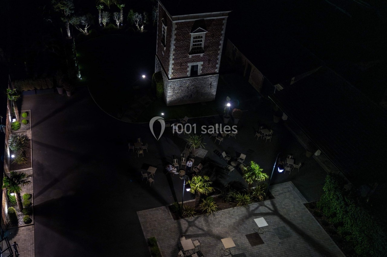 Vue aérienne nocturne d'une cour éclairée avec des tables, des chaises et un bâtiment en briques.
