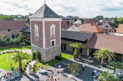 Vue aérienne d'une cour avec une tour en briques, des bâtiments anciens, des palmiers et des personnes réunies.