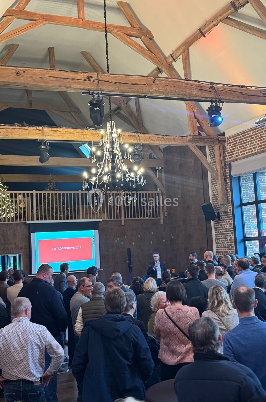 Un groupe de personnes assiste à une présentation dans une salle avec poutres apparentes et un écran projeté.