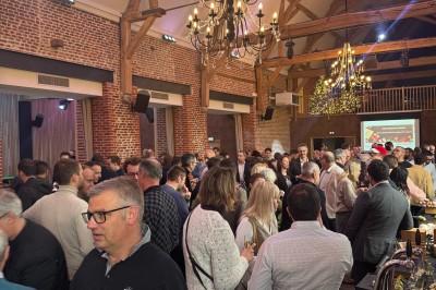 SUV vert exposé dans une salle avec parquet et murs en bois, accompagné de panneaux promotionnels en arrière-plan.