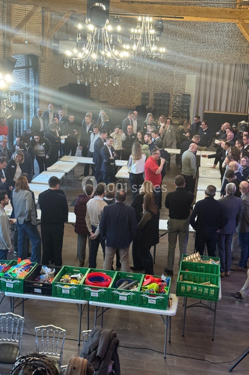 Des personnes rassemblées dans une salle avec des tables, des jouets et des caisses vertes au premier plan.