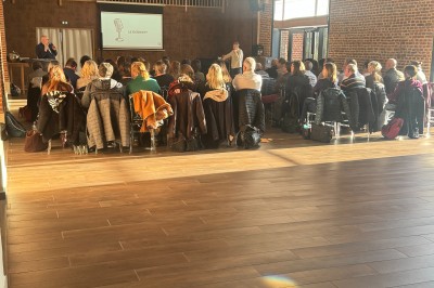 SUV vert exposé dans une salle avec parquet et murs en bois, accompagné de panneaux promotionnels en arrière-plan.