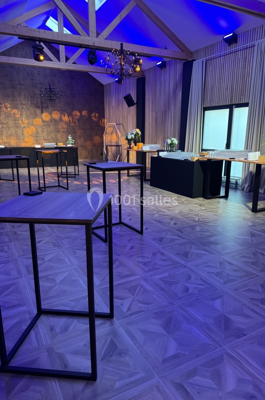 Salle de réception moderne avec tables hautes, décoration élégante, éclairage bleu et grandes fenêtres.