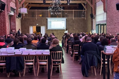 SUV vert exposé dans une salle avec parquet et murs en bois, accompagné de panneaux promotionnels en arrière-plan.