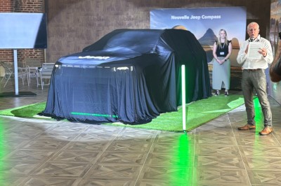 SUV vert exposé dans une salle avec parquet et murs en bois, accompagné de panneaux promotionnels en arrière-plan.