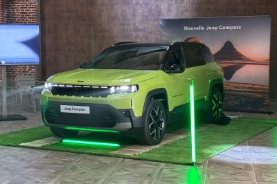 SUV vert exposé dans une salle avec parquet et murs en bois, accompagné de panneaux promotionnels en arrière-plan.