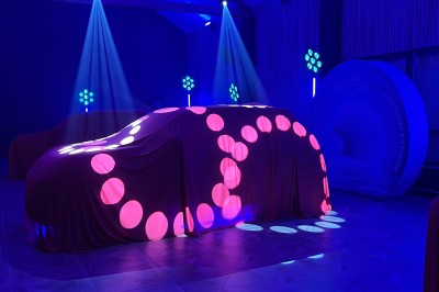 SUV vert exposé dans une salle avec parquet et murs en bois, accompagné de panneaux promotionnels en arrière-plan.