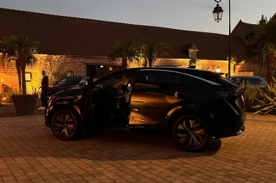 SUV vert exposé dans une salle avec parquet et murs en bois, accompagné de panneaux promotionnels en arrière-plan.