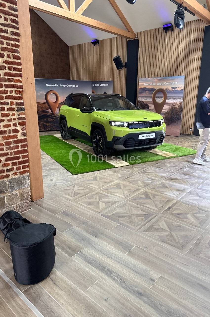 SUV vert exposé dans une salle avec parquet et murs en bois, accompagné de panneaux promotionnels en arrière-plan.