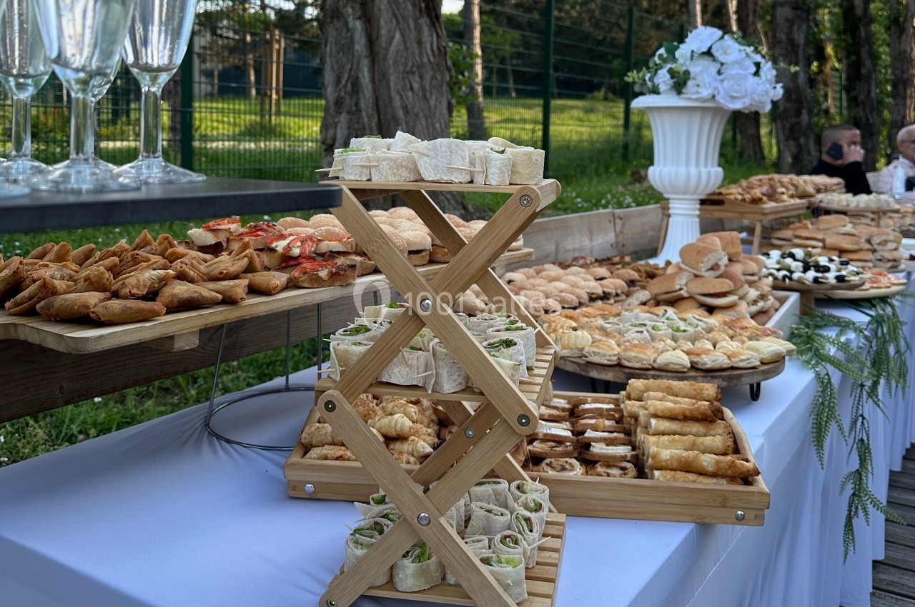 Buffet en plein air avec une variété de bouchées salées, disposées sur des plateaux en bois près d'un jardin.