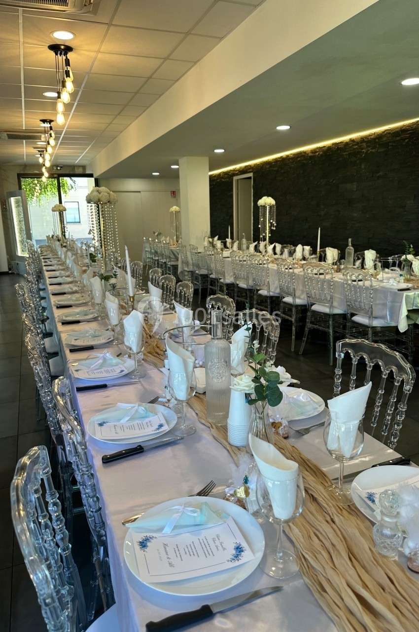 Salle de réception décorée avec des tables longues, nappes blanches, chaises transparentes et centres de table élégants.