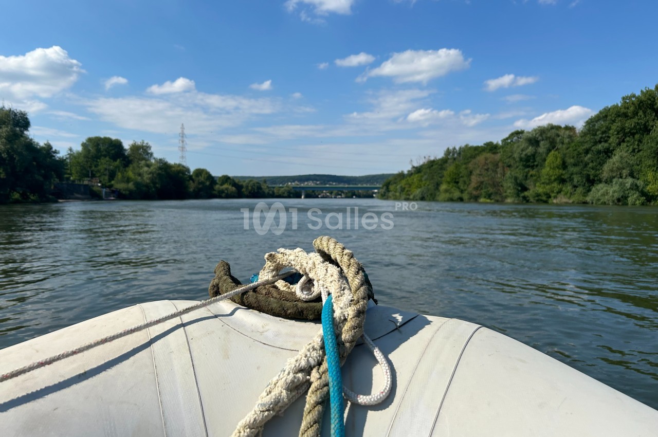 Vue depuis un bateau pneumatique sur une rivière bordée de végétation, sous un ciel partiellement nuageux.