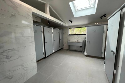 Sanitaires modernes avec cabines fermées, lavabo, carrelage clair et lumière naturelle provenant d'une fenêtre et d'un puits…