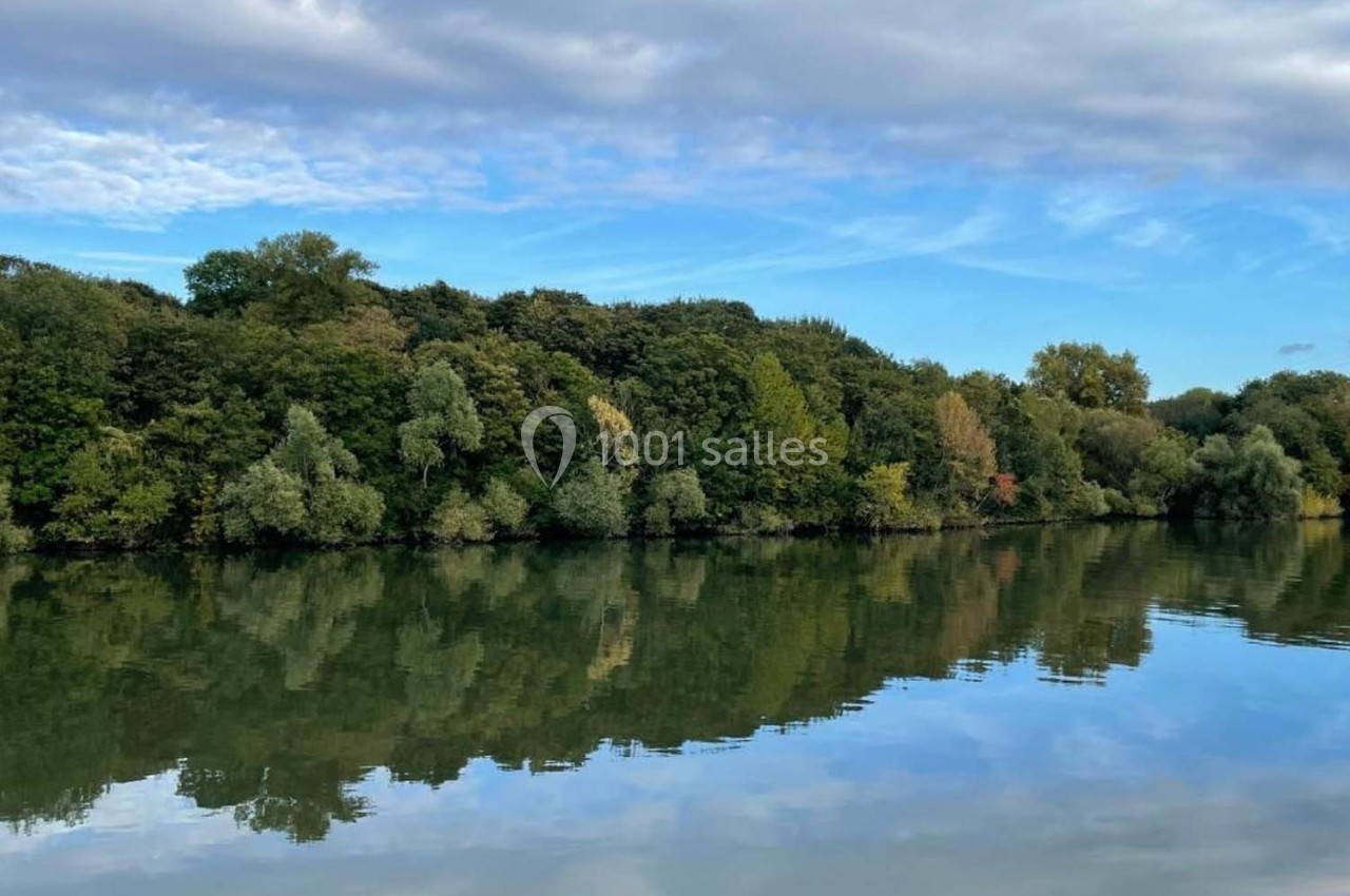 Rivière calme reflétant une rangée d'arbres et un ciel partiellement nuageux.