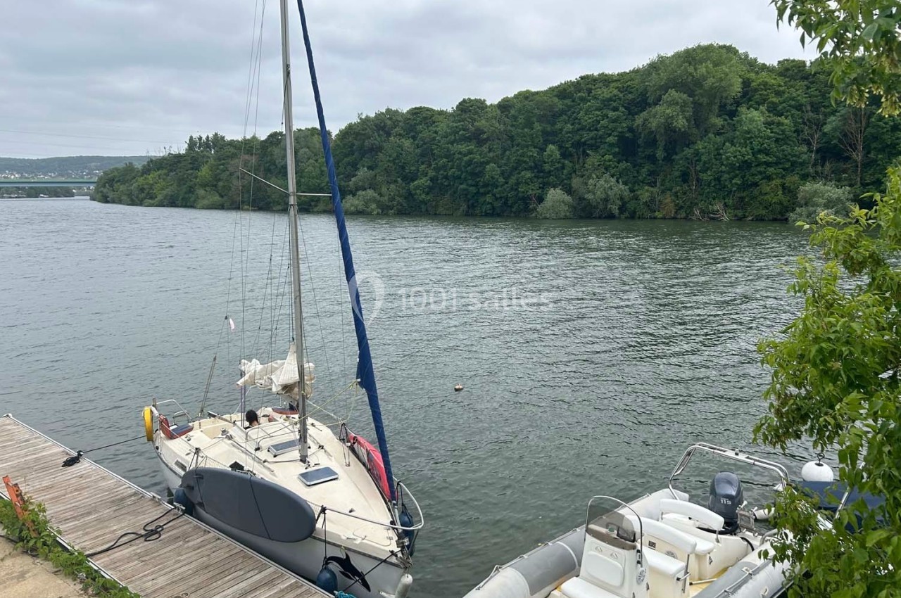 Deux bateaux amarrés à un ponton en bois sur une rivière bordée de végétation dense.